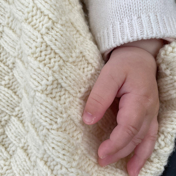 La main d'un bébé, posée sur une couverture 100% laine mérinos.