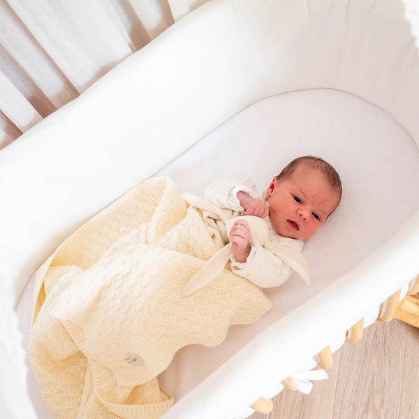 Un bébé est dans son berceau, enveloppé d'une couverture en pure laine mérinos.
